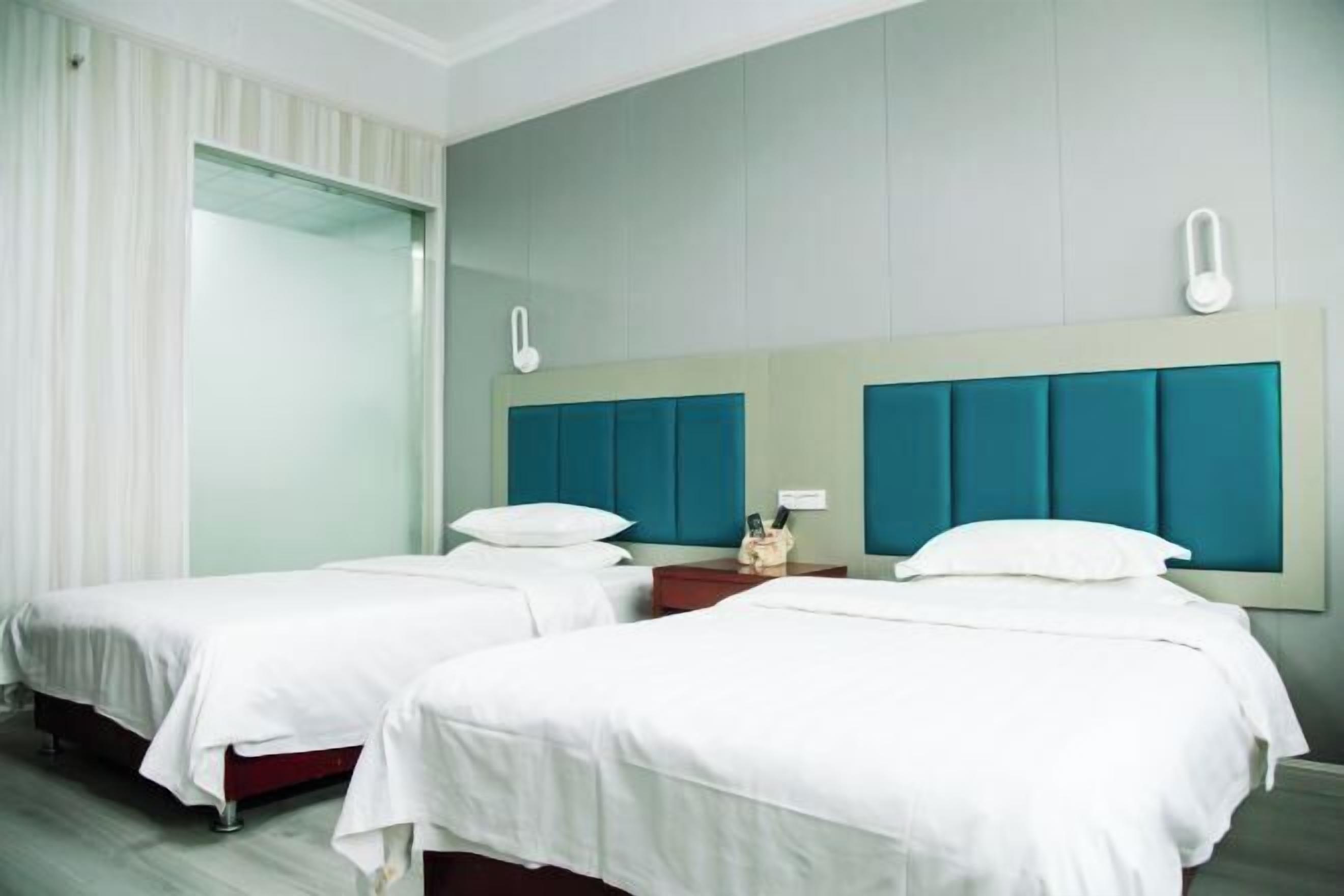 A hotel room with two beds, a large window with curtains, and a teal-colored headboard.