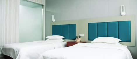 A hotel room with two beds, a large window with curtains, and a teal-colored headboard.