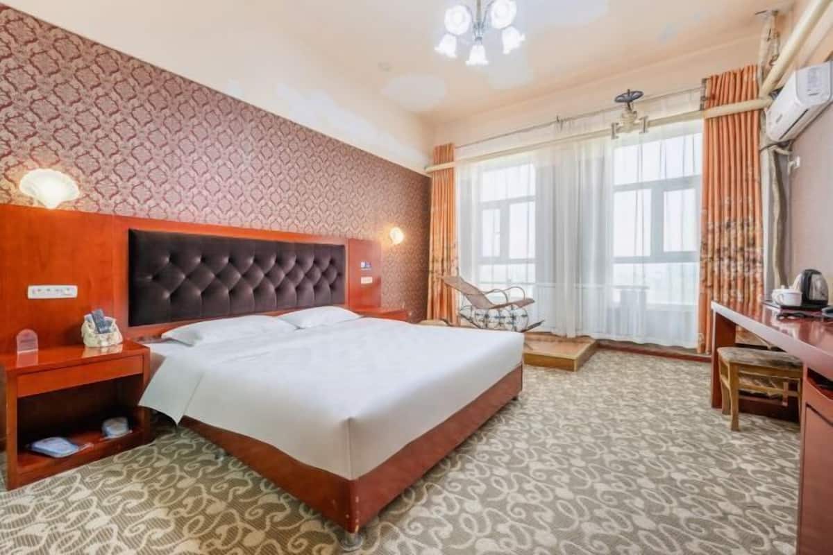 A hotel room with a large bed, a wooden nightstand, a desk, and a chair.
