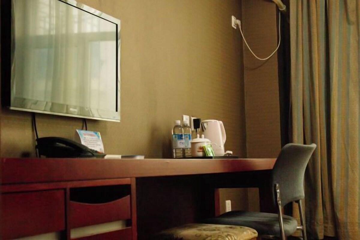 Hotellihuone, jossa on puinen työpöytä, televisio, puhelin, kahvinkeitin ja tuoli.