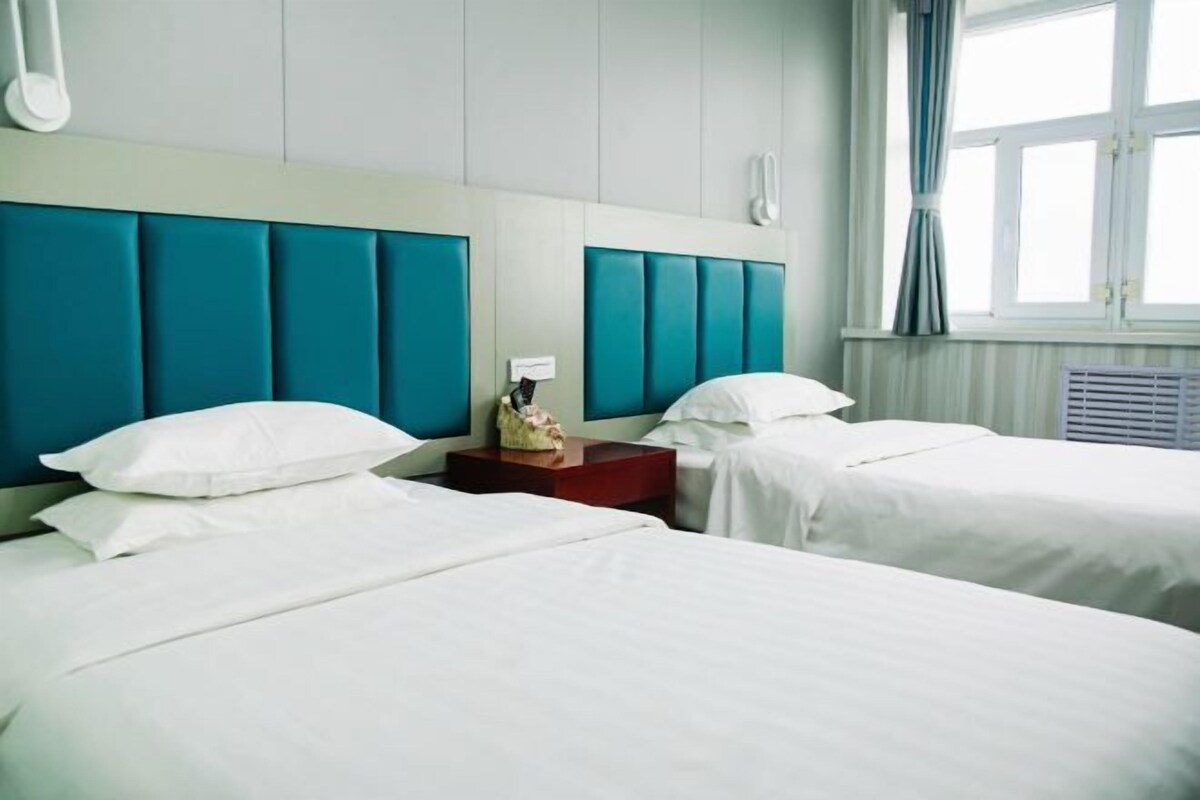 Hotellihuone, jossa on kaksi sänkyä, puinen yöpöytä ja ikkuna, jossa on verhot.