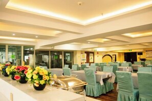 Een restaurantgedeelte in een hotel met tafels, stoelen, een buffet en een receptiebalie.