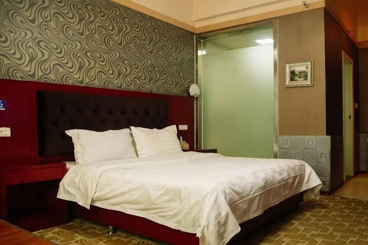 A hotel room with a bed, a nightstand, a wall clock, a door, and a patterned wall.