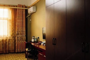 A room with a desk, chair, wardrobe, and an air conditioning unit.