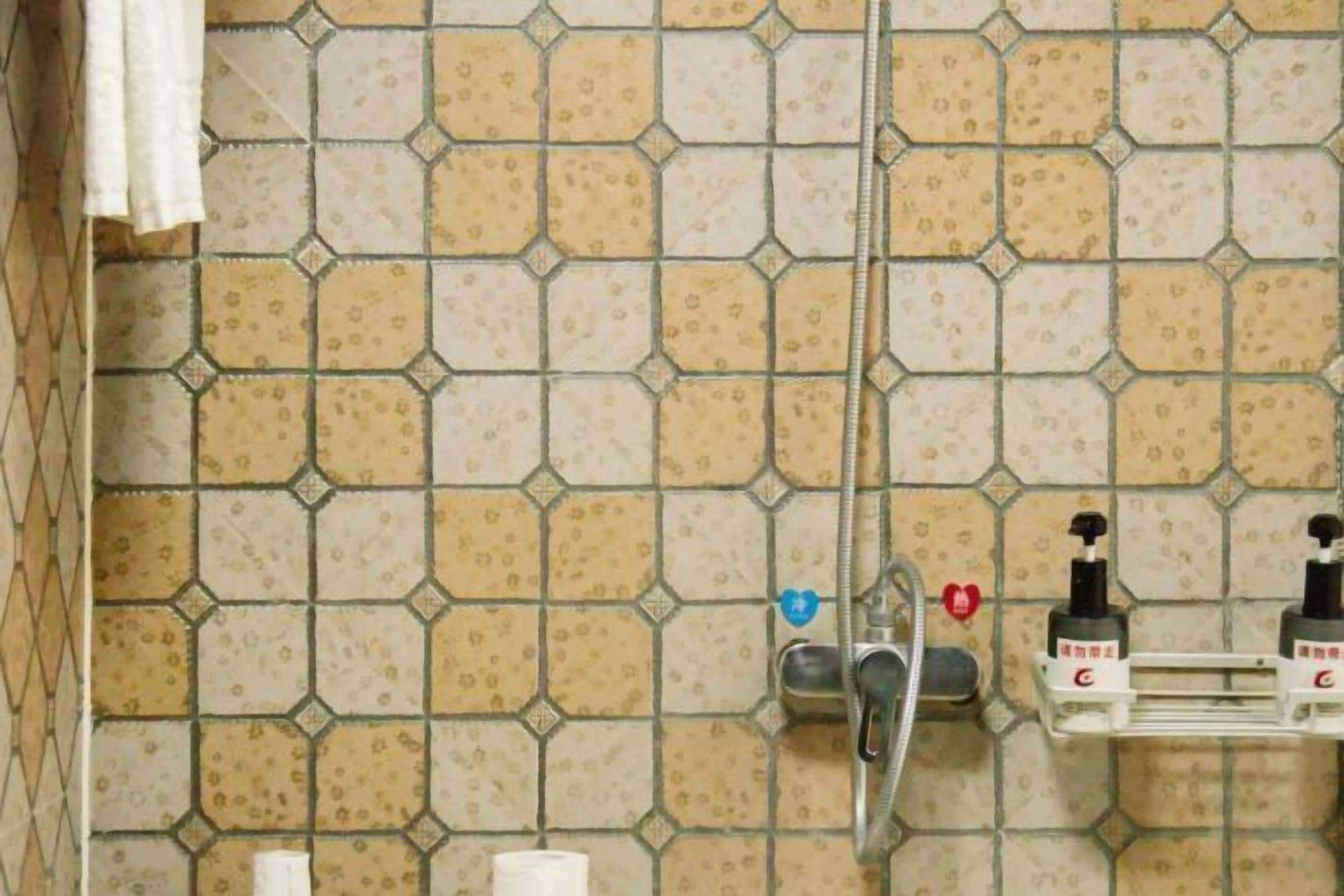A bathroom with hexagonal patterned tiles, a showerhead, a soap dispenser, and a towel rack.