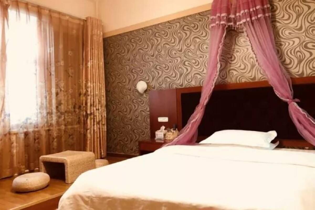 A hotel room with a large bed, a nightstand, a small stool, and a decorative wall pattern.