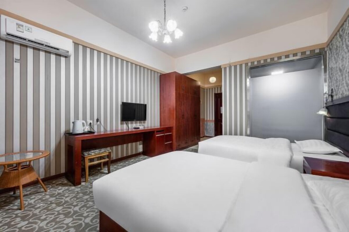 Hotellihuone, jossa on kaksi sänkyä, työpöytä, jossa on televisio, kahvinkeitin ja vaatekaappi.