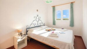 A neatly made bed with a white bedspread, a bedside table with a lamp, and a window with curtains. - Monte Majore House 70B, Porto Rotondo, Italy (Porto Rotondo)