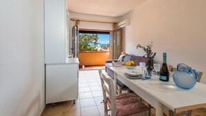 A dining area with a table set for two, a refrigerator, and a view of the outdoors. - Monte Majore House 70B, Porto Rotondo, Italy (Porto Rotondo)