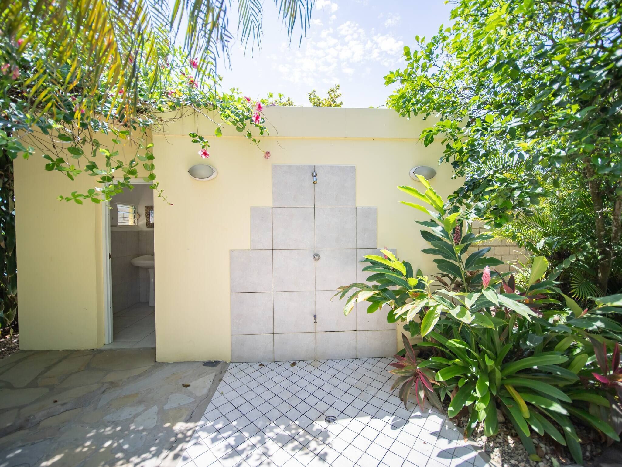 A small, enclosed outdoor area with a tiled floor, a wall-mounted sink, and various plants.