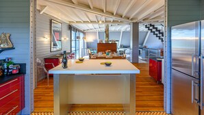 A modern kitchen with a central island, wooden flooring, and a stainless steel refrigerator.