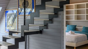 A modern interior with a staircase, a bed with teal bedding, and a framed picture on the wall.