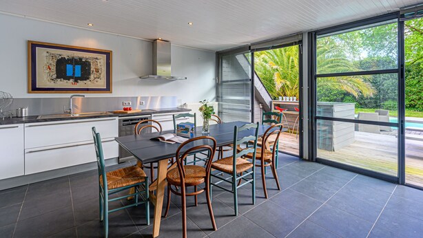 A modern kitchen with a dining area, large windows, and a view of a pool.