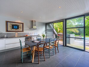 A modern kitchen with a dining area, large windows, and a view of a pool. - Villa Pyramide II by Interhome (Saint Philibert)