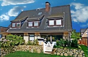 Een huis met twee verdiepingen, een schuin dak, een stenen muur en een witte picket hek.