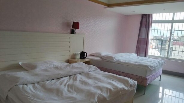 Una habitación de hotel con dos camas, una mesita de noche con lámpara y una ventana con vistas.