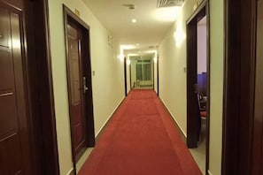 En hotellkorridor med en röd matta, trädörrar och utsikt in i ett rum med en lila vägg.