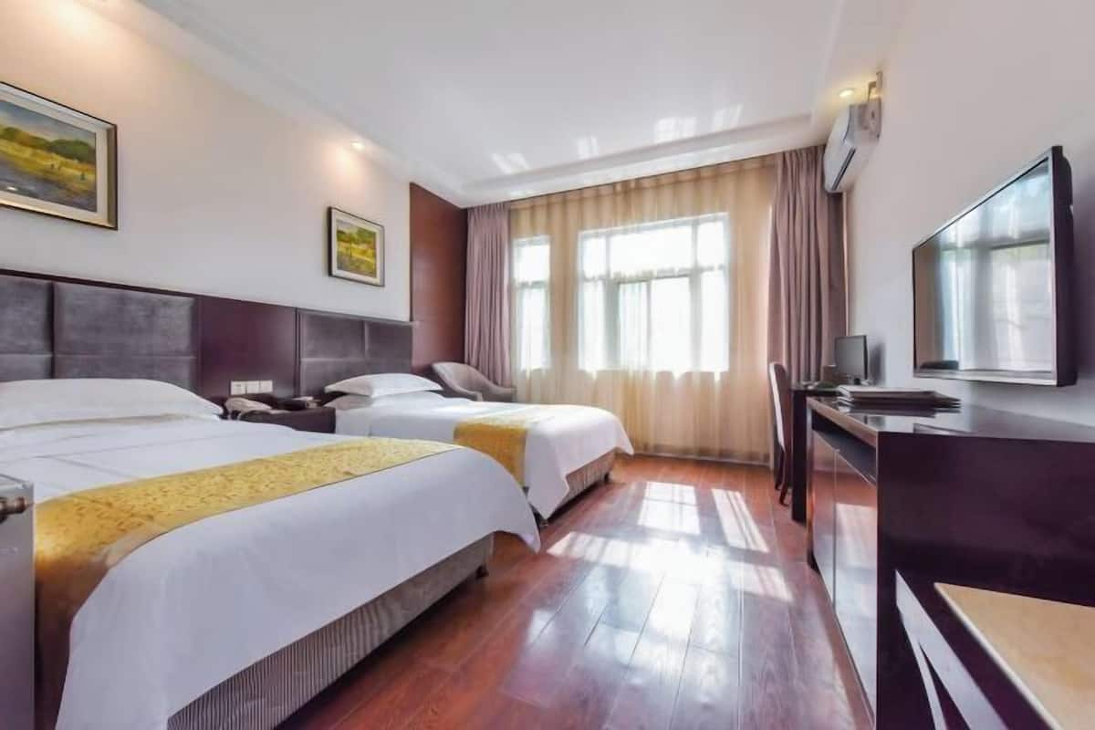 A hotel room with two beds, a desk, a television, and a large window with curtains.