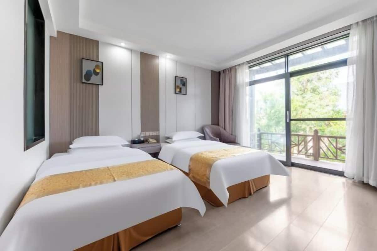A hotel room with two beds, a desk, a chair, and a balcony with a view.