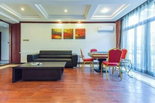 Uma sala moderna com sofá, mesa de centro e área de jantar com cadeiras. Há três quadros na parede e uma grande janela com cortinas.