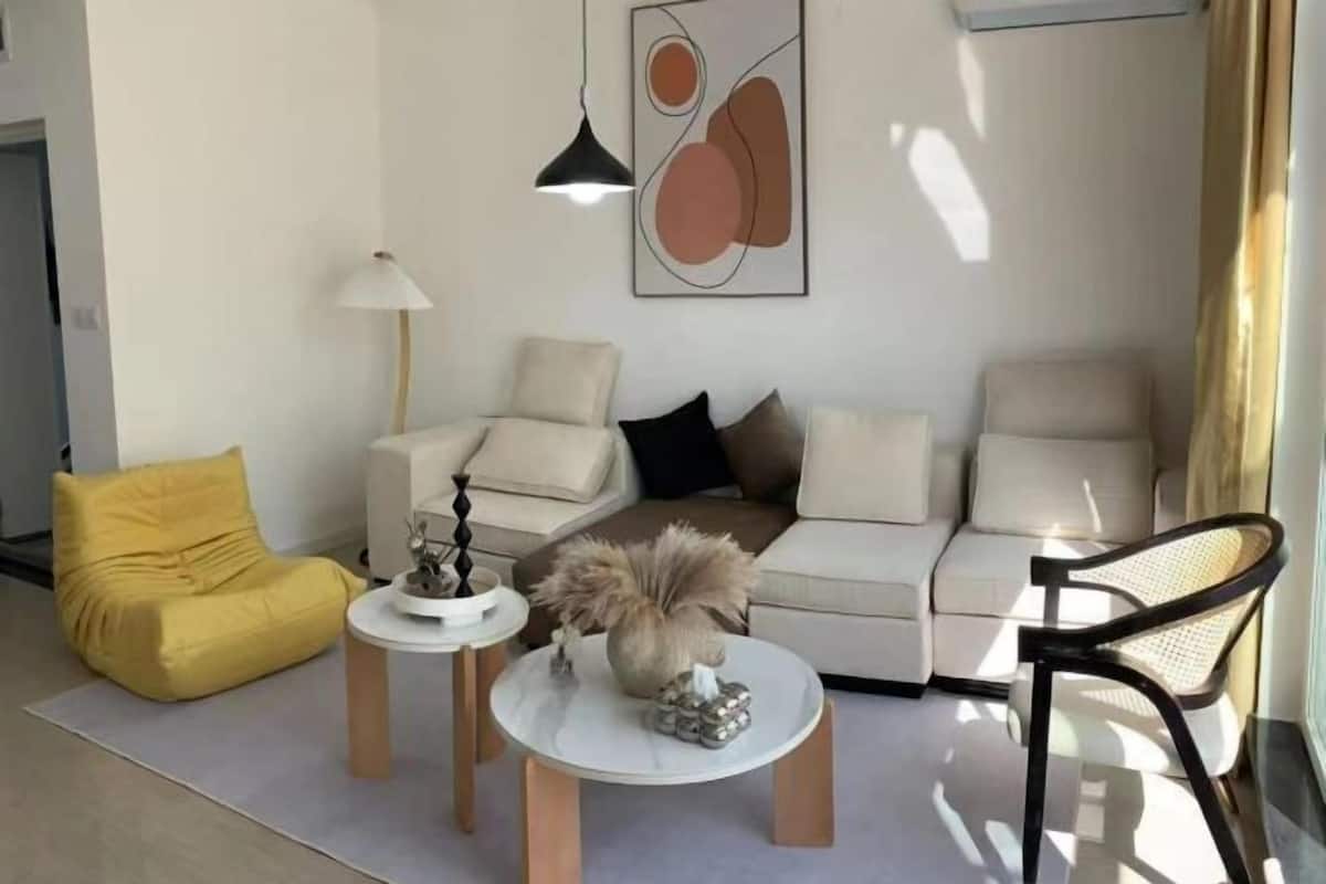 A modern living room with a sofa, yellow bean bag, and a coffee table with decorative items.
