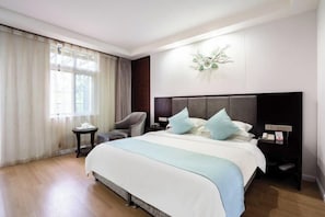 Une chambre d’hôtel avec un grand lit, une chaise, une table de chevet et un luminaire fixé au mur.