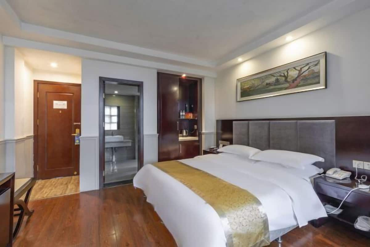 A hotel room with a bed, a nightstand, a telephone, a painting on the wall, and a door leading to a bathroom.