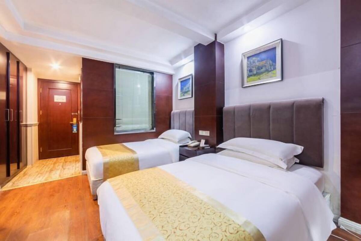 A hotel room with two beds, a wooden floor, a window, and a painting on the wall.