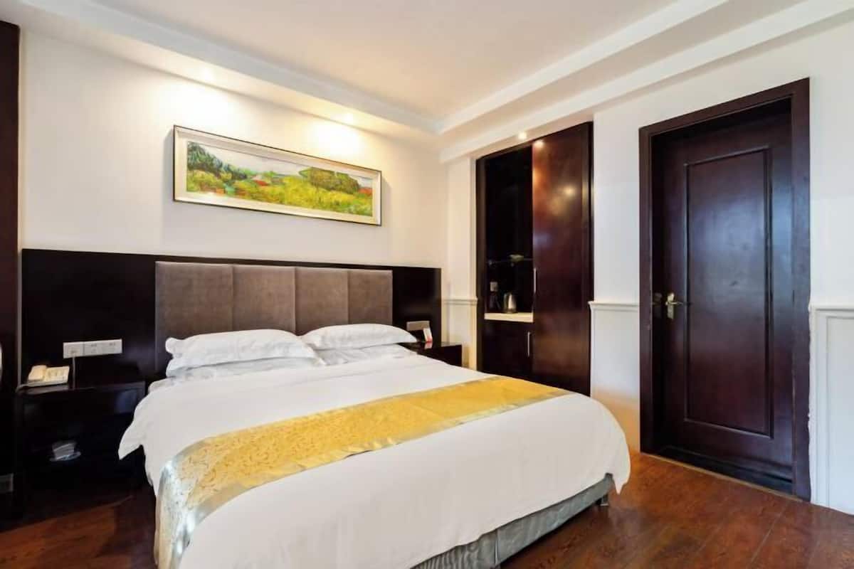 A hotel room with a large bed, dark wood headboard, a painting on the wall, and two dark wooden doors.