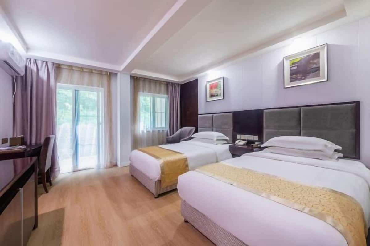 A hotel room with two beds, a desk, a chair, and a window with curtains.