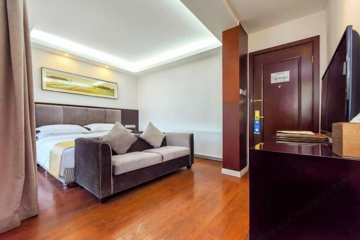A hotel room with a bed, a sofa, a desk, and a door.