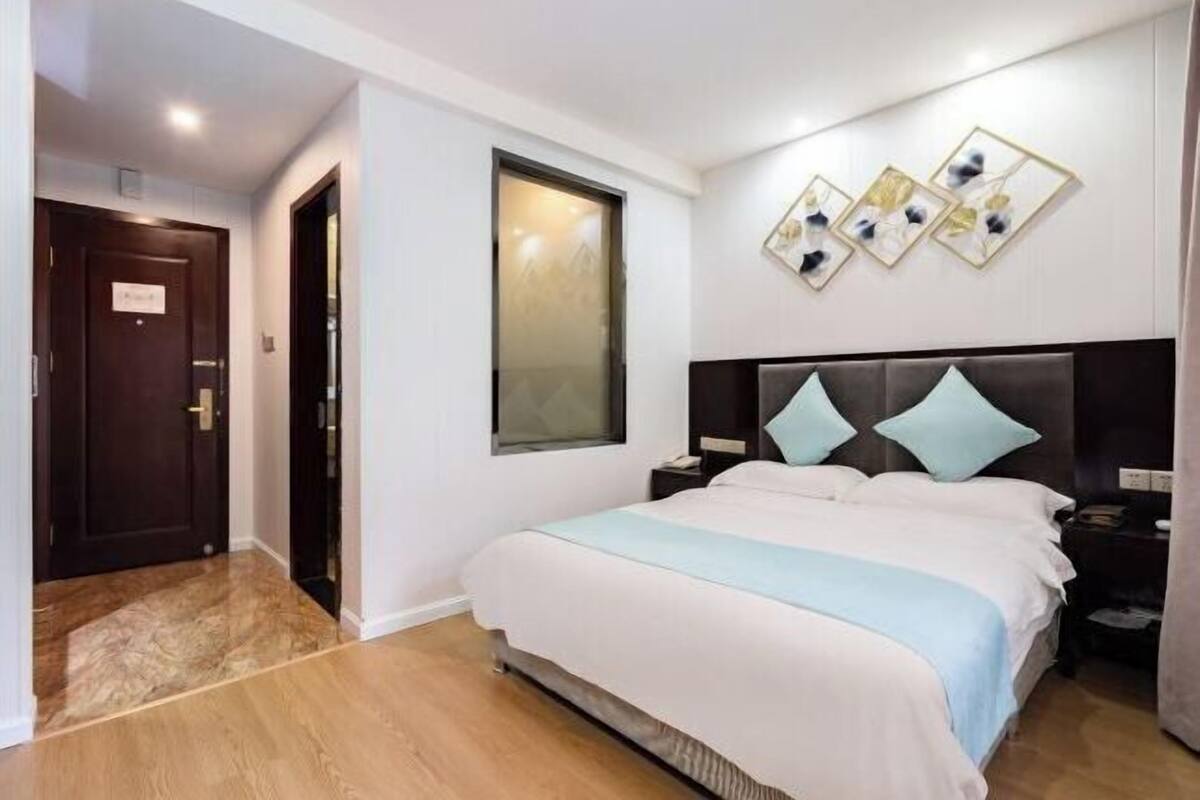 A hotel room with a bed, a nightstand, a window, and a door.