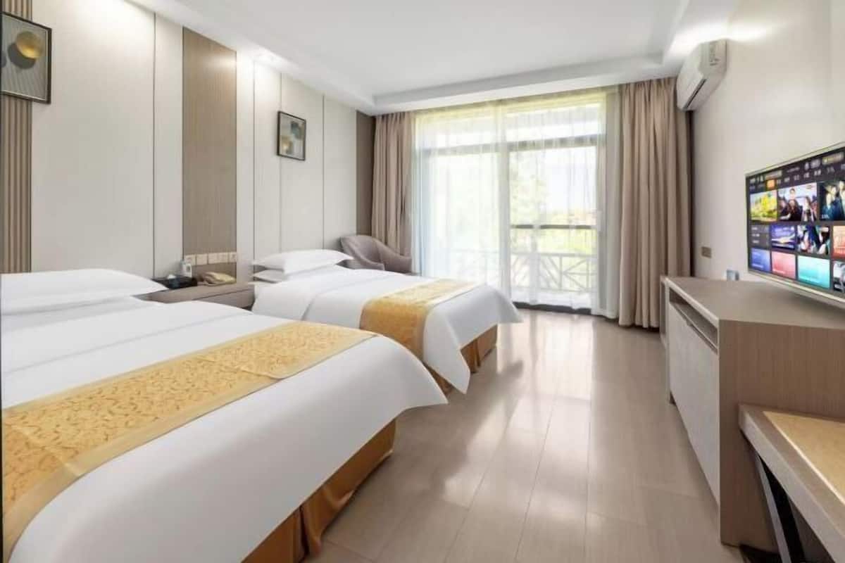 A hotel room with two beds, a desk, a TV, and a balcony with curtains.