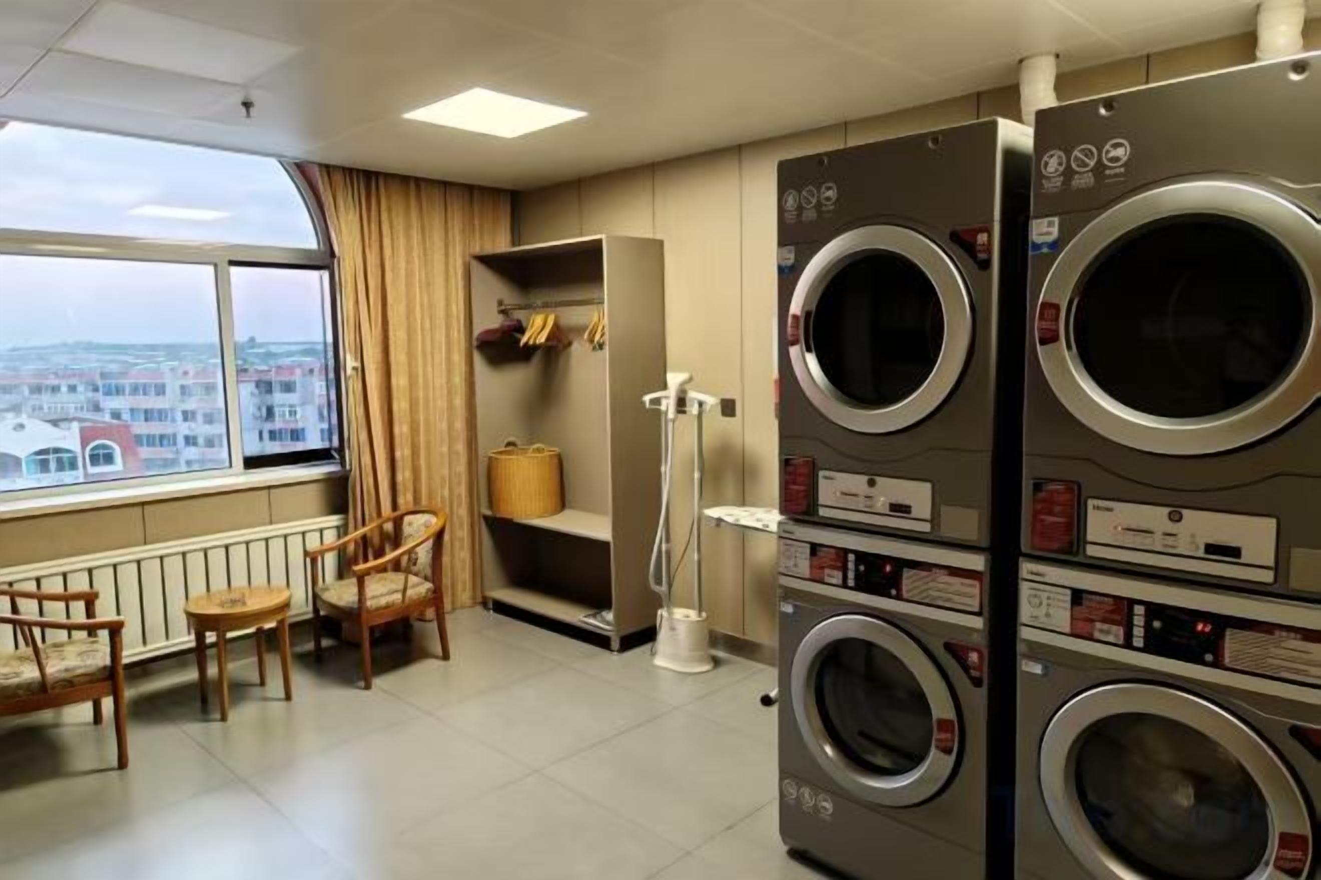 A laundry room with stacked washing machines, a drying rack, and a view of the city through a large window.