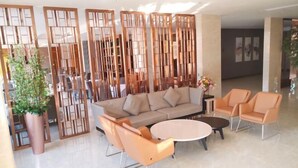 A modern living room with a beige sofa, orange armchairs, a round coffee table, and a decorative wooden partition. - Dalian yuanfeng hotel (Dalian)