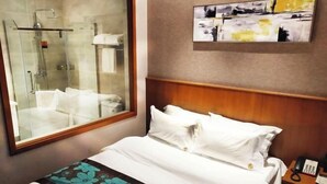 A hotel room with a bed, a nightstand with a phone, a shower area, and a painting on the wall. - Dalian yuanfeng hotel (Dalian)