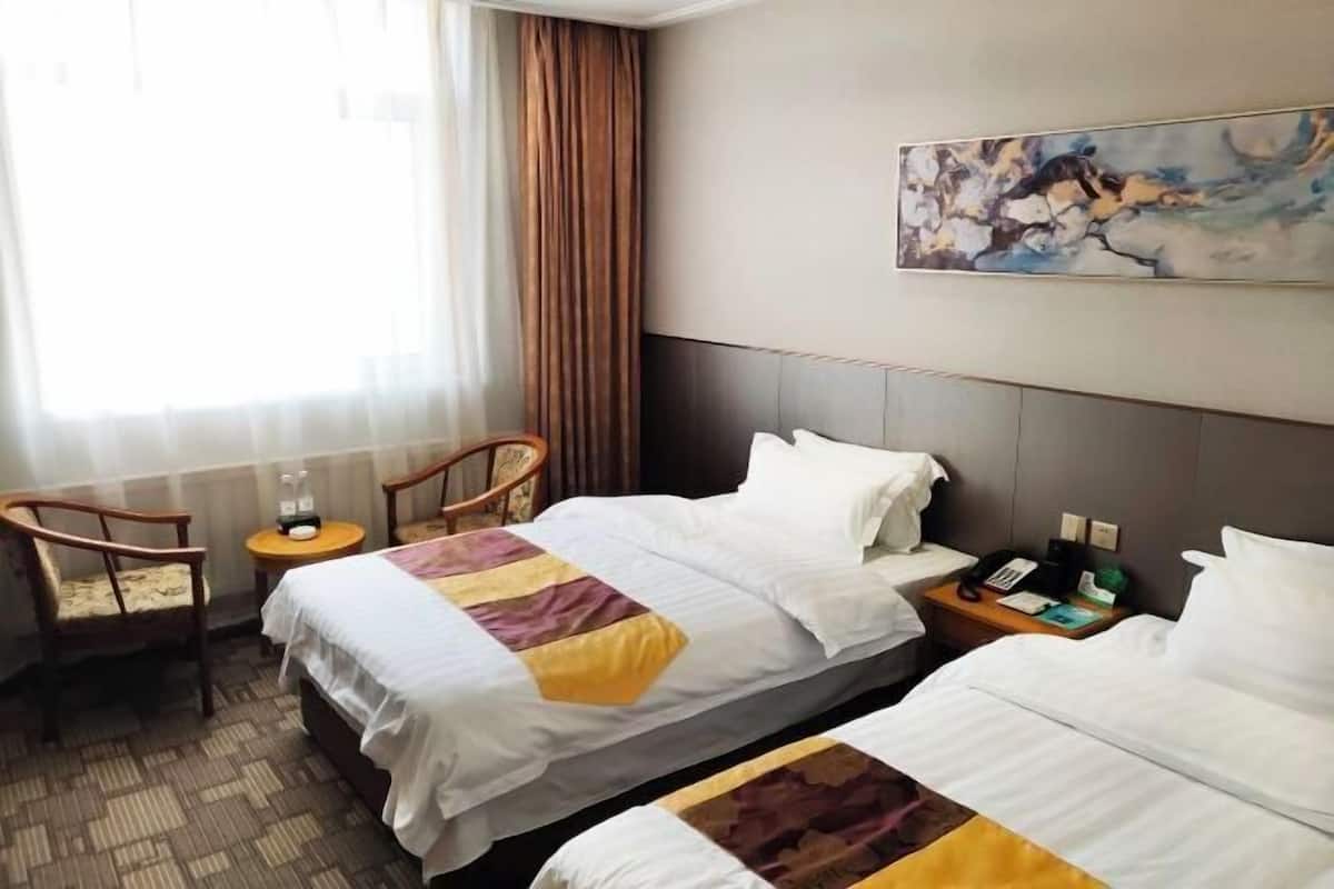 A hotel room with two beds, a chair, a small table, and a painting on the wall.