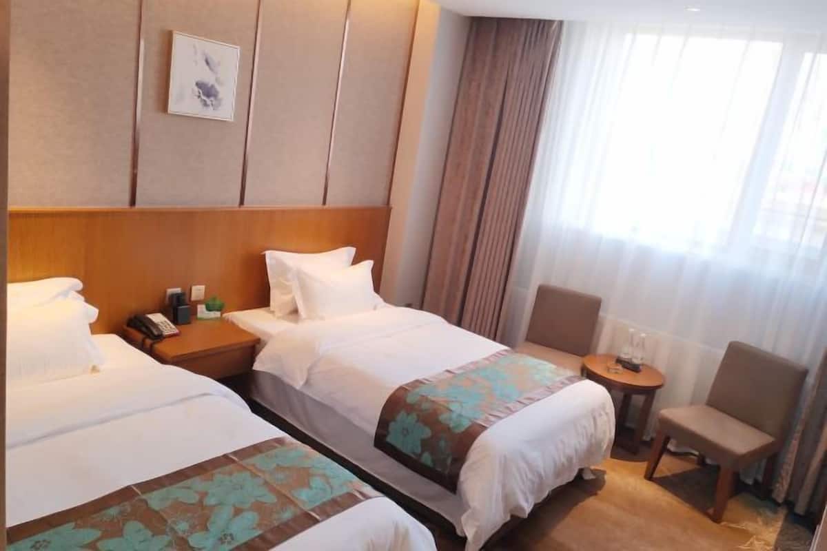 A hotel room with two beds, a small table, a chair, and a window with curtains.