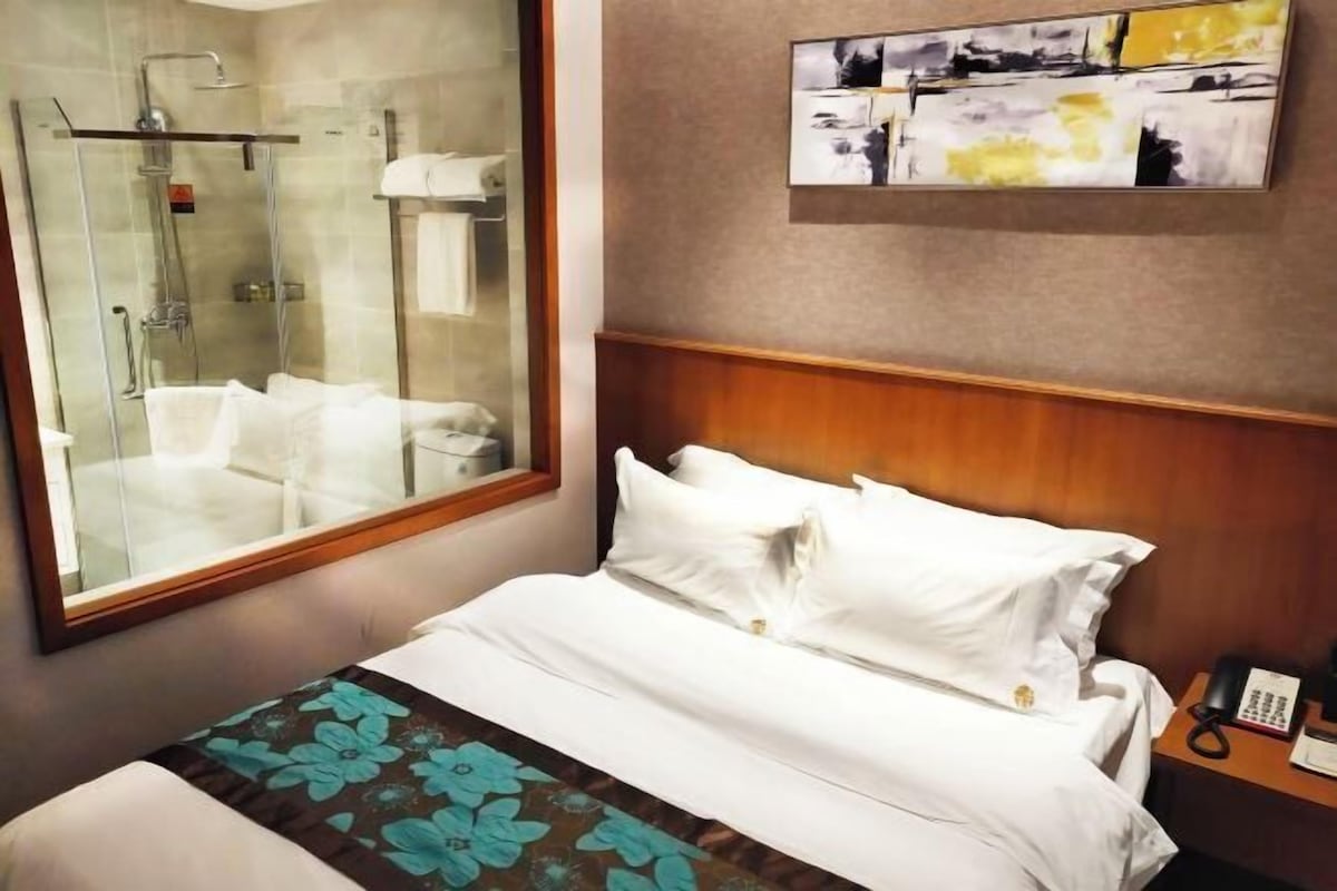 A hotel room with a bed, a shower, and a painting on the wall.