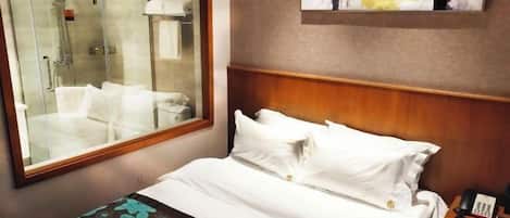 A hotel room with a bed, a shower, and a painting on the wall.