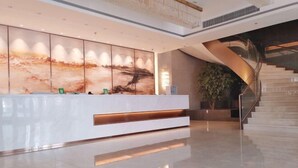 A modern reception area with a white reception desk, a large abstract painting on the wall, and a curved staircase. - Dalian yuanfeng hotel (Dalian)