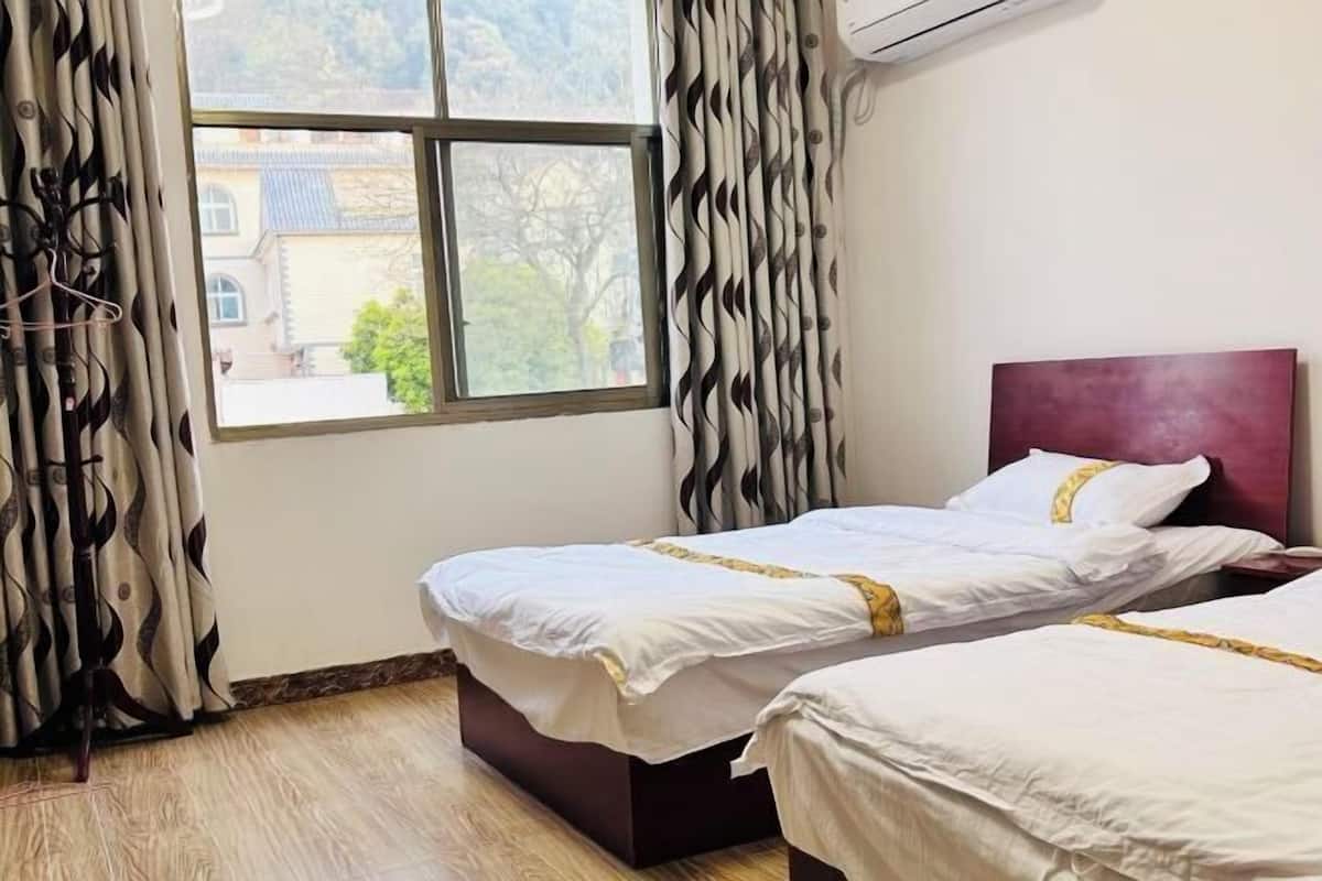 A hotel room with two beds, a window with curtains, and a view of a building outside.
