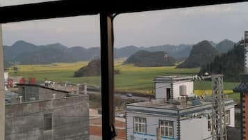 Vista a través de una ventana que muestra un edificio con una torre de agua, un pequeño edificio blanco con techo azul, y una estructura metálica a la derecha.
