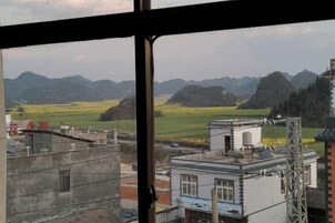 Vista a través de una ventana que muestra un edificio con una torre de agua, un pequeño edificio blanco con techo azul, y una estructura metálica a la derecha.