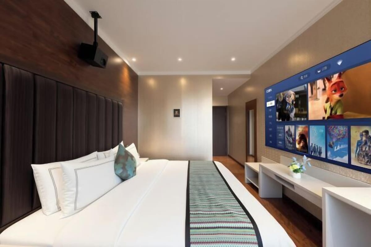 A modern hotel room with a large bed, a flat-screen TV mounted on the wall, and a desk with a chair.