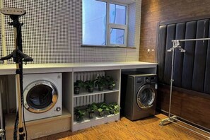 A compact laundry area with a washing machine, dryer, and shelving for plants. - SANDOU Hotel (Hohhot Vientiane City Dazhao Square) (Hohhot)