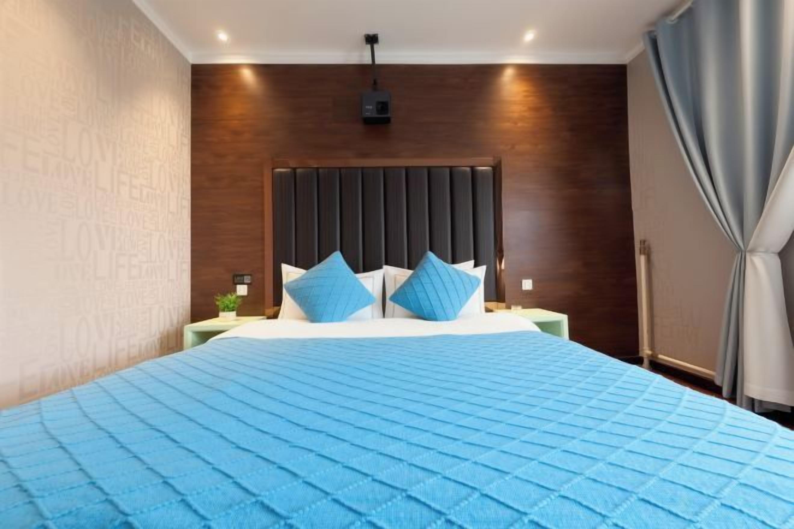 Quarto moderno com uma cama grande, cabeceira escura e colcha azul.