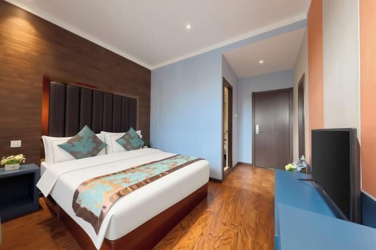 A modern hotel room with a large bed, a flat-screen TV, and a wooden floor.