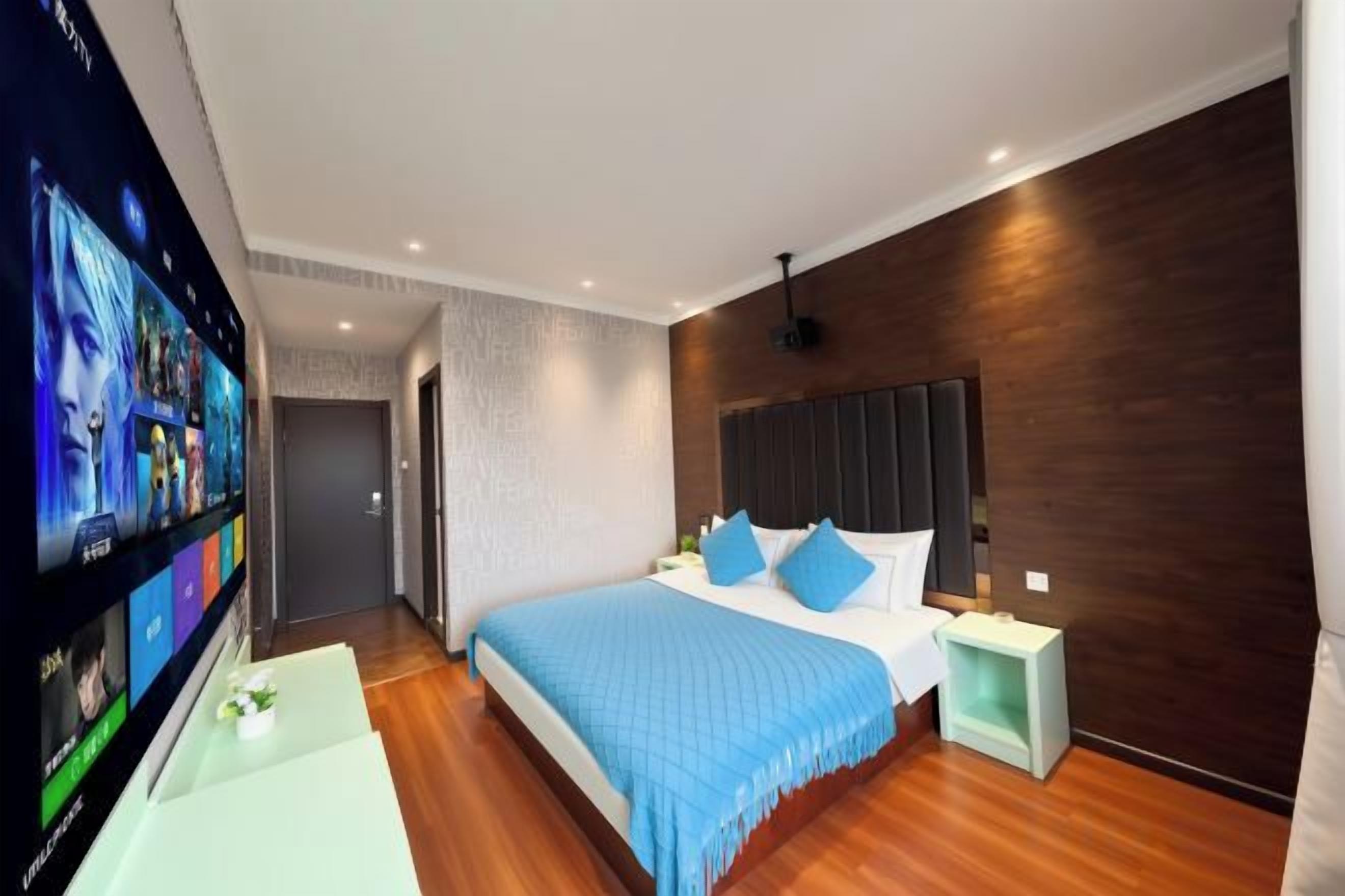 A modern hotel room with a large bed, a TV on the left, and a wooden floor.