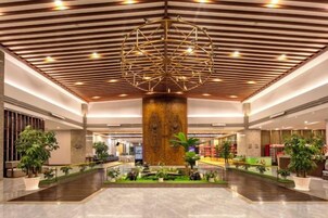 A spacious lobby with a central column, potted plants, and a modern ceiling design.